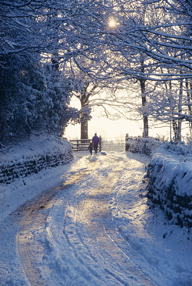 Man and child walking down a snow covered road in winter near Arthington, West Yorkshire, England, United Kingdom, Europe