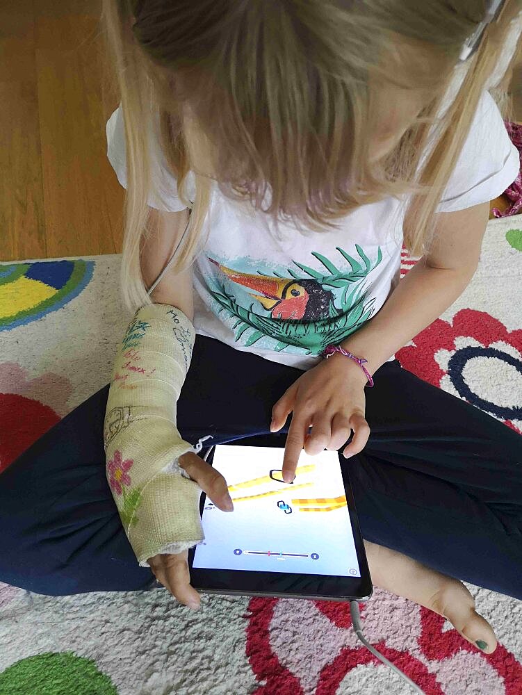 8 year old girl with broken wrist, platree, playing a game on a touch pad, European, France.