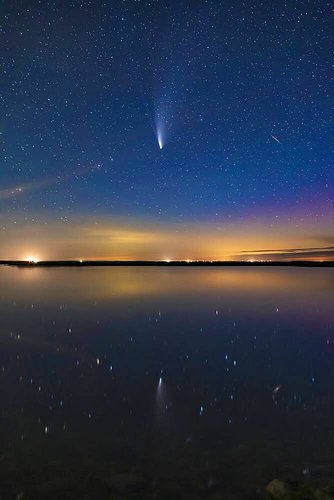 Comet NEOWISE (C/2020 F3) reflected in the still waters this night of Crawling Lake in southern Alberta. A dim aurora at right colours the sky magenta. Lingering twilight colours the sky blue. A meteor or more likely a flaring satellite appears at right and is also reflected in the water. Even in this short exposure, the two tails ' dust and ion ' are visible. This was July 20, 2020.