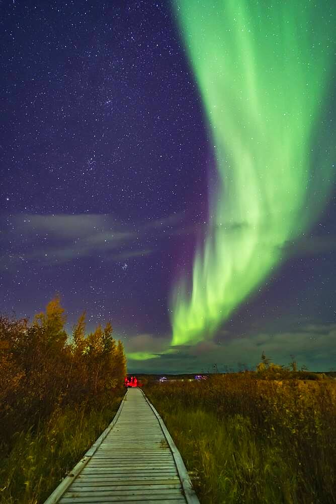 A aurora group is taking their aurora selfie shots on the boardwalk at Rotary Park in Yellowknife, NWT, under a grand sweep of an auroral arc. This was September 11, 2018 under a mild display of Lights. Illumination is from the aurora and from urban lighting nearby.