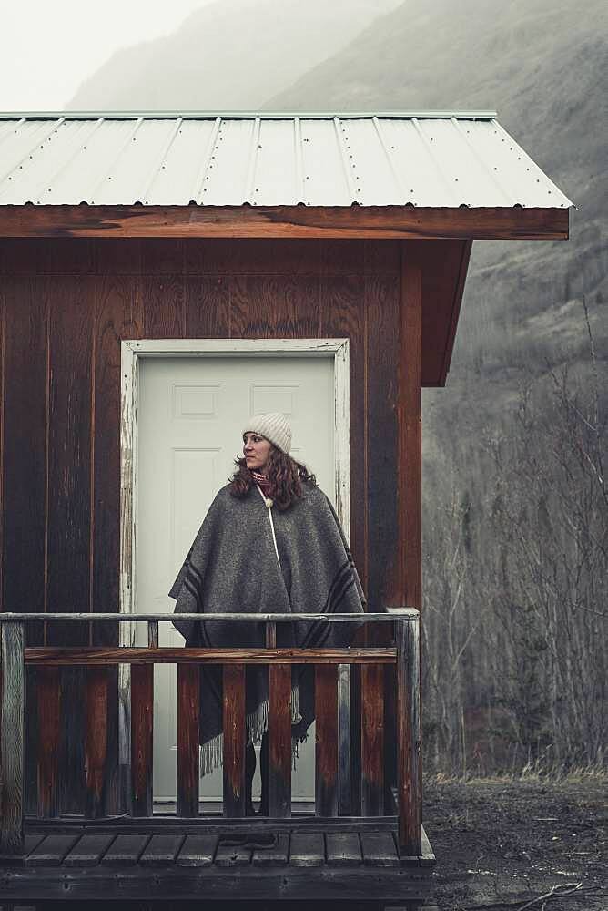 An attractive Woman with stands in front of her cabin and lets her eyes wander across the cold surroundings. Yukon Territory, Canada