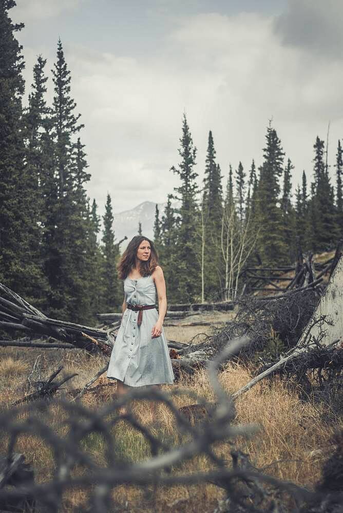 An attractive young woman walks in her jeansdress over an abandoned grazing ground in the bush. Yukon Territory, Canada