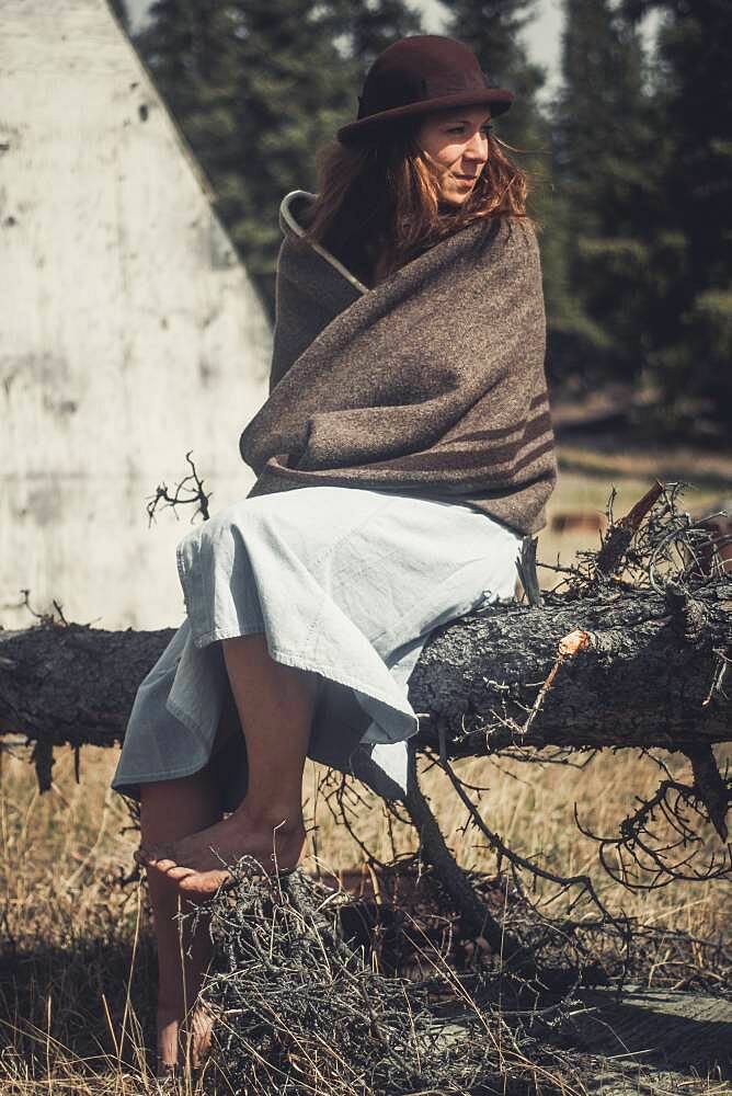 An attractive young woman sits on a log wrapped in a woollen blanket. Yukon Territory, Canada