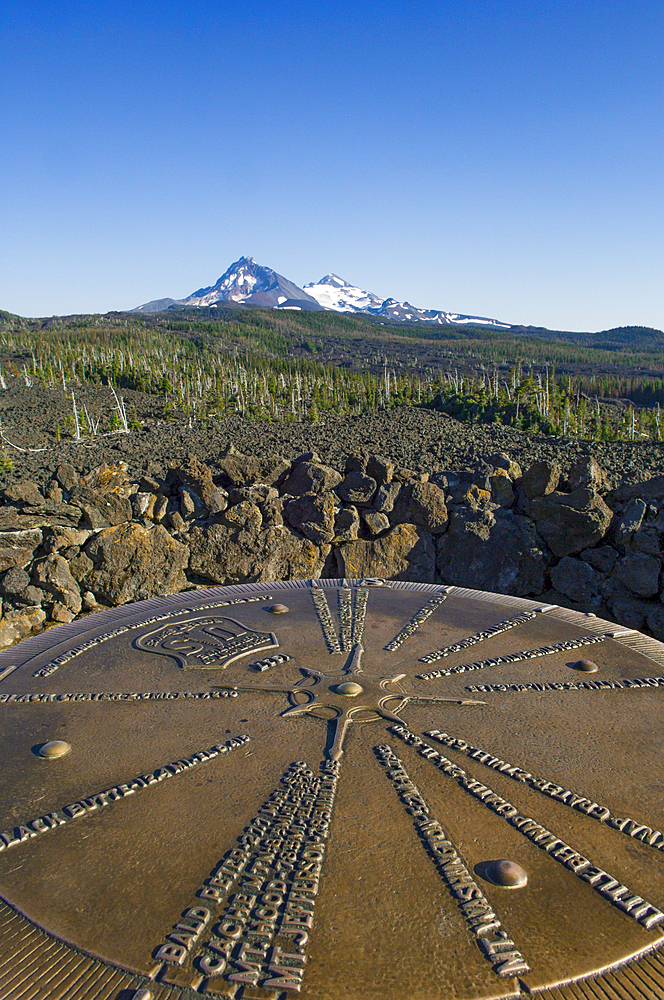 Bronze plaque pointing out mountain peaks seen from Dee Wright Observatory at McKenzie Pass in the Cascade Mountains of Oregon, with North Sister and Middle Sister volcanic peaks in the distance.