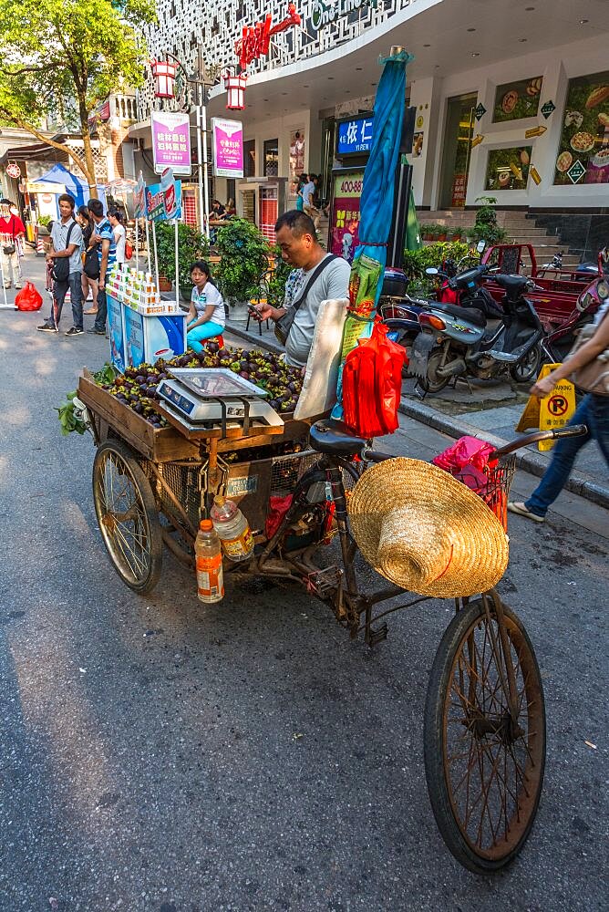 A vendor sells mangosteen fruit from a three-wheeled bike cart on the street in Guilin, China.