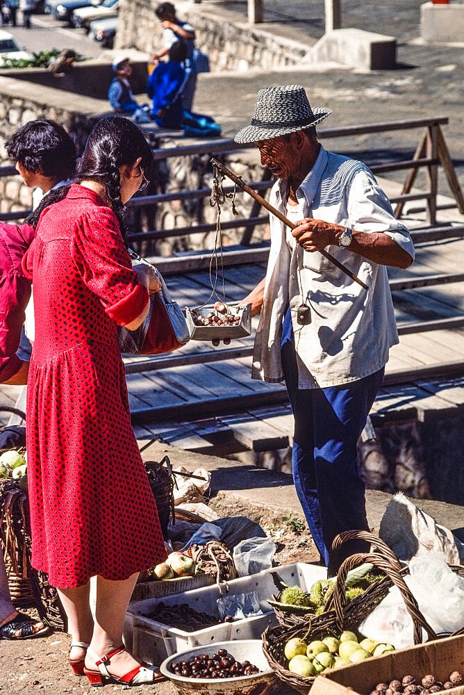 A vendor weighing produce with a hand balance scale in the farmers market in Mutianyu, China