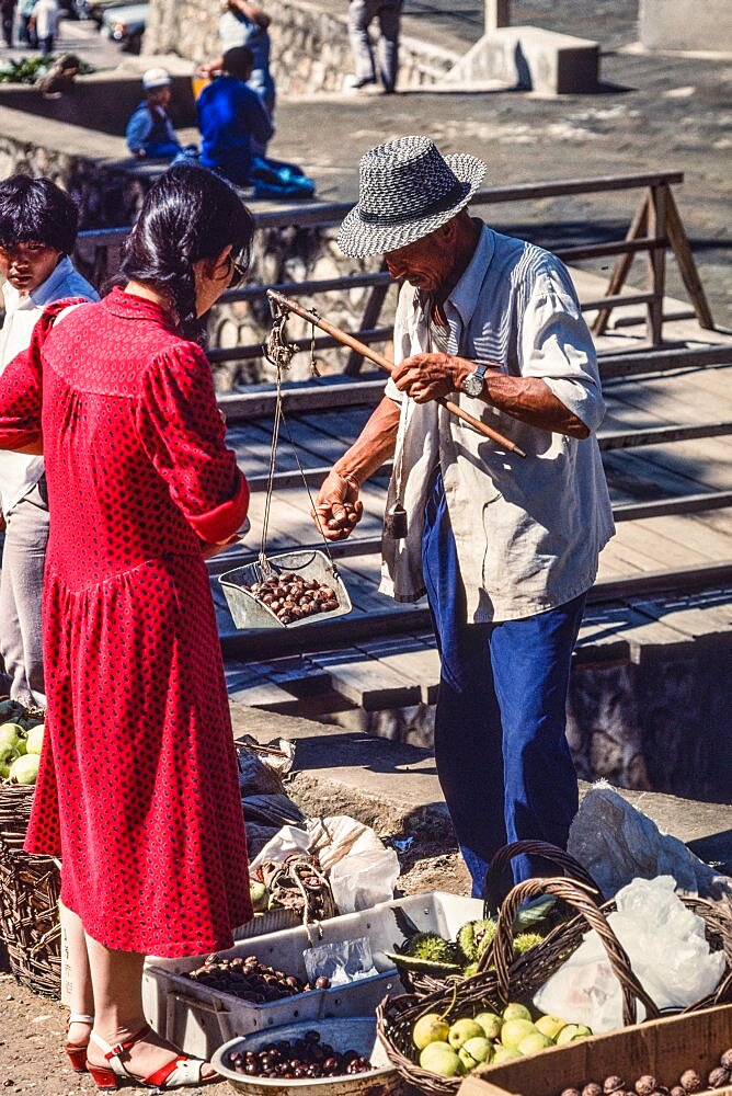 A vendor weighing produce with a hand balance scale in the farmers market in Mutianyu, China