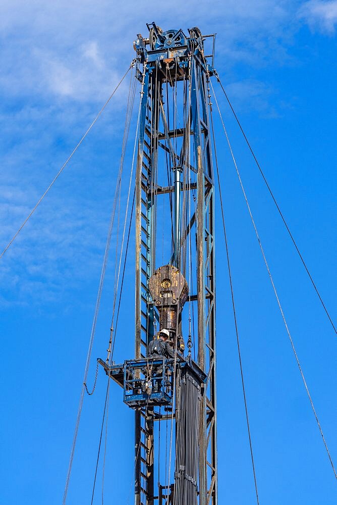 The derrickhand or derrickman working in the rod basket on the mast of an oil field workover rig.