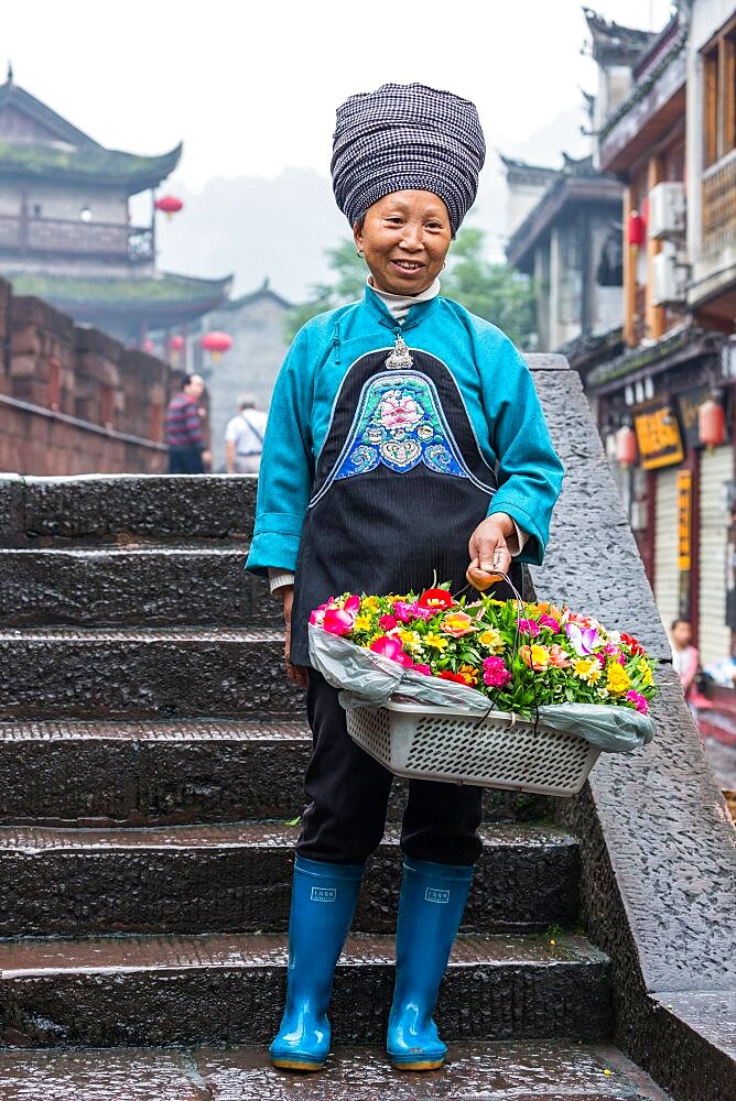 A woman in the traditional attire of the Tujia ethnic minority selling flowers in Fenghuang, China.