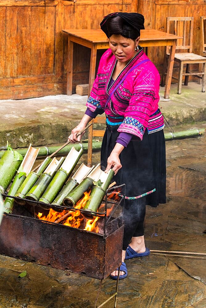 A Red Yao woman cooking rice in bamboo tubes over an open fire in Jinking, Longshen, China.