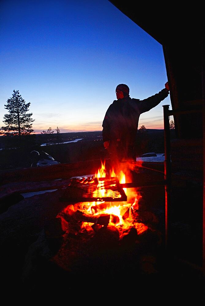 Jânkâlâ relaxes by the fire during a stop. Snowmobile sunset tour with Arctic Lifestyle, Rovaniemi, Lapland, Finland.