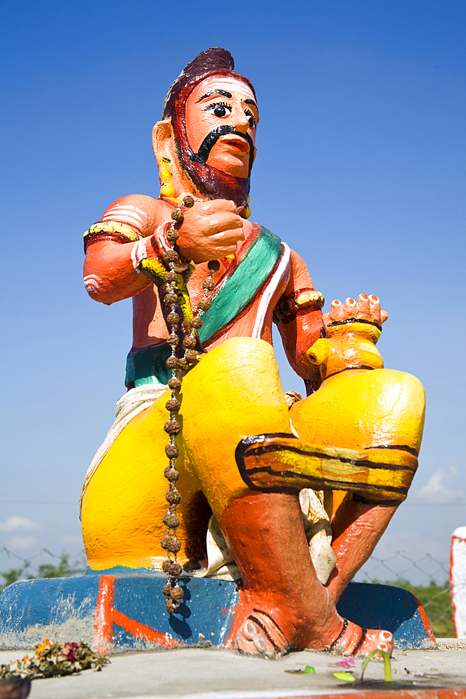 Colourful religious statue depicting man sitting on wall at a Hindu Shrine, Tamil Nadu, India