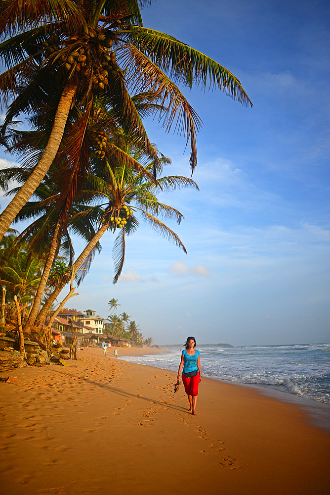 Young woman walking on Hikkaduwa beach at sunset, Sri Lanka