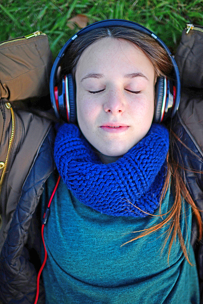 Cute teenager listening to music with headphones in park