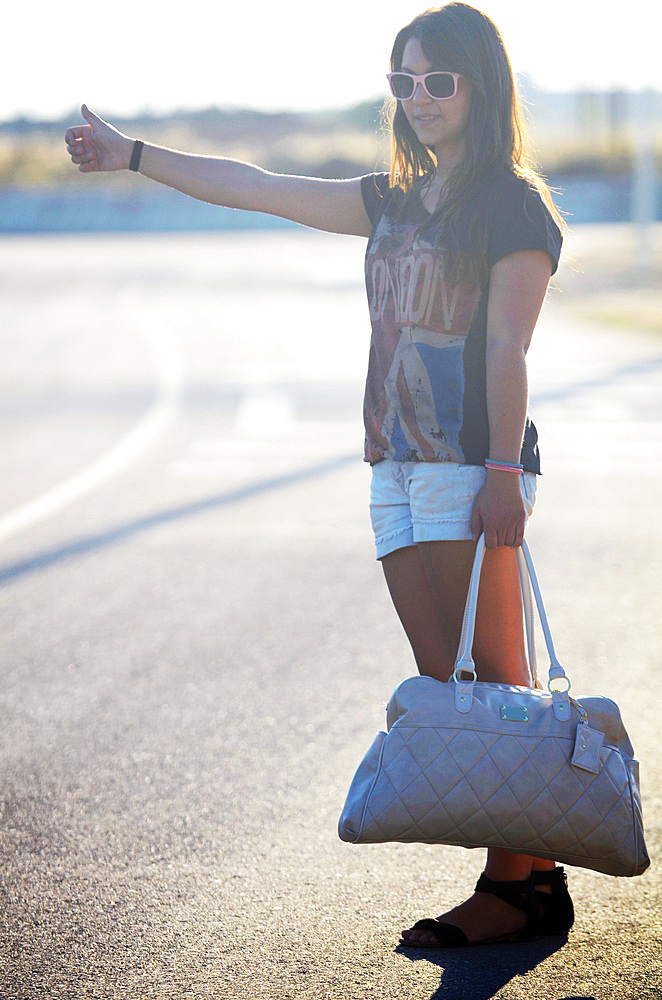 Young cute woman hitchhiking at sunset