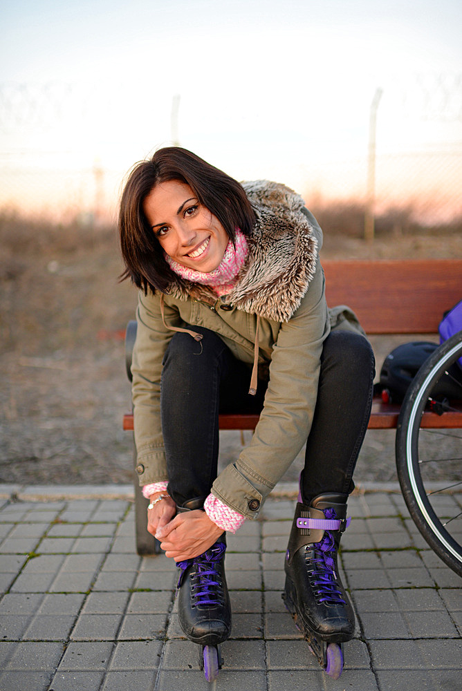 Young attractive woman puts rollerblades on at sunset