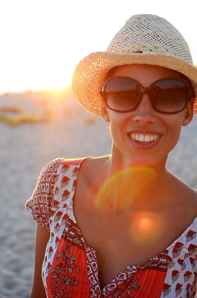 Young woman with straw hat on the beach at sunset