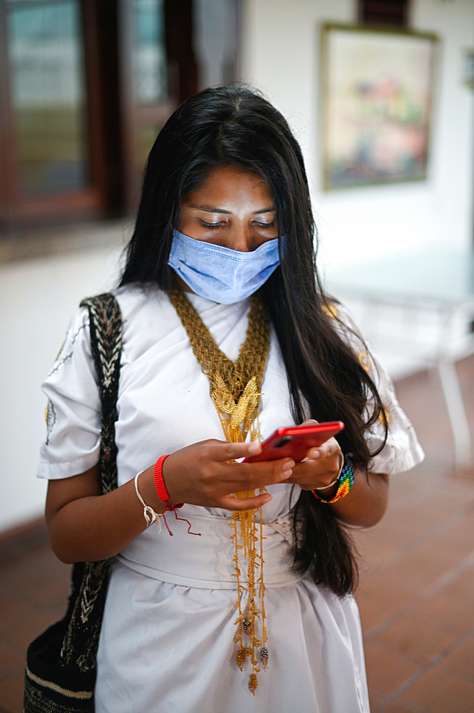 Portrait of young Arhuaco indigenous woman wearing a face mask and using her smartphone during the Covid-19 outbreak in Colombia