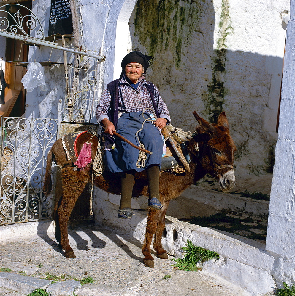 Portrait of an old woman sitting on a donkey in a village in Greece, Europe