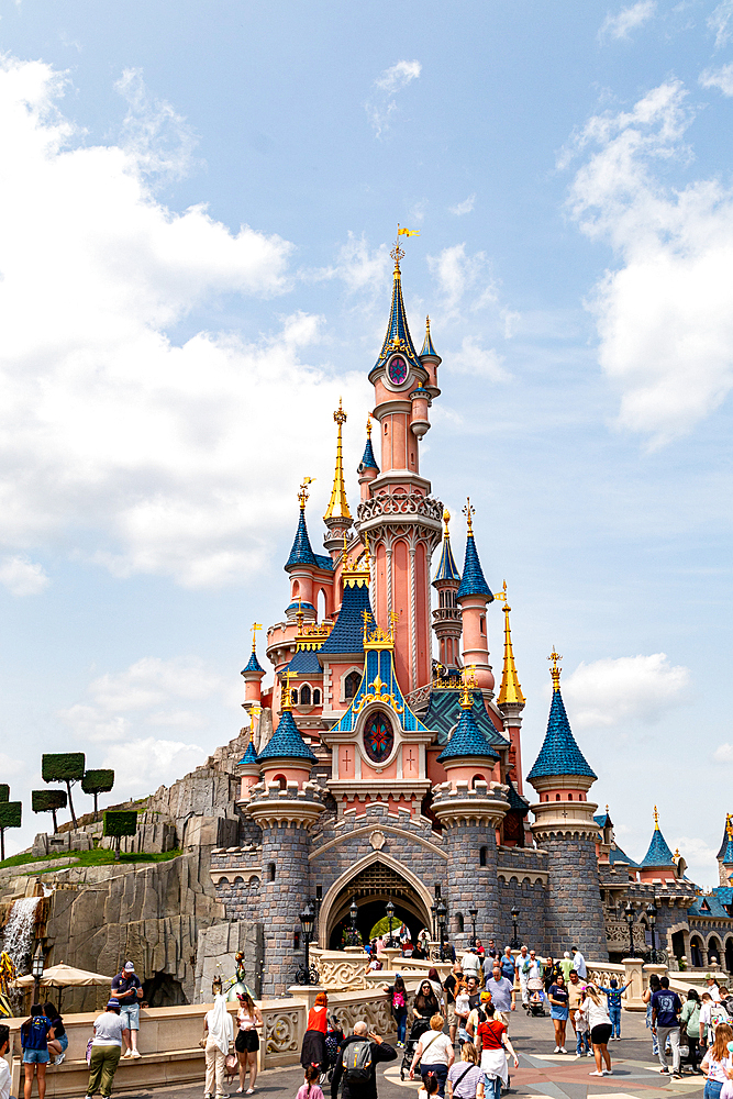 Full shot of Disneyland Paris’ castle, with a crowd of people in front and a blue sky with clouds in the background.