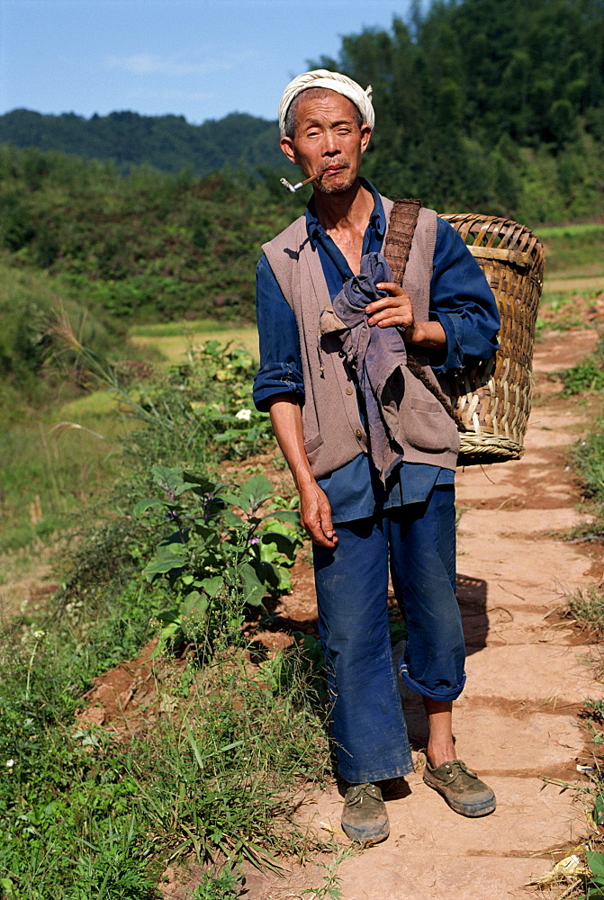 Portrait of a peasant with pipe, typical white head band, carrying a wicker basket, in Sichuan, China, Asia