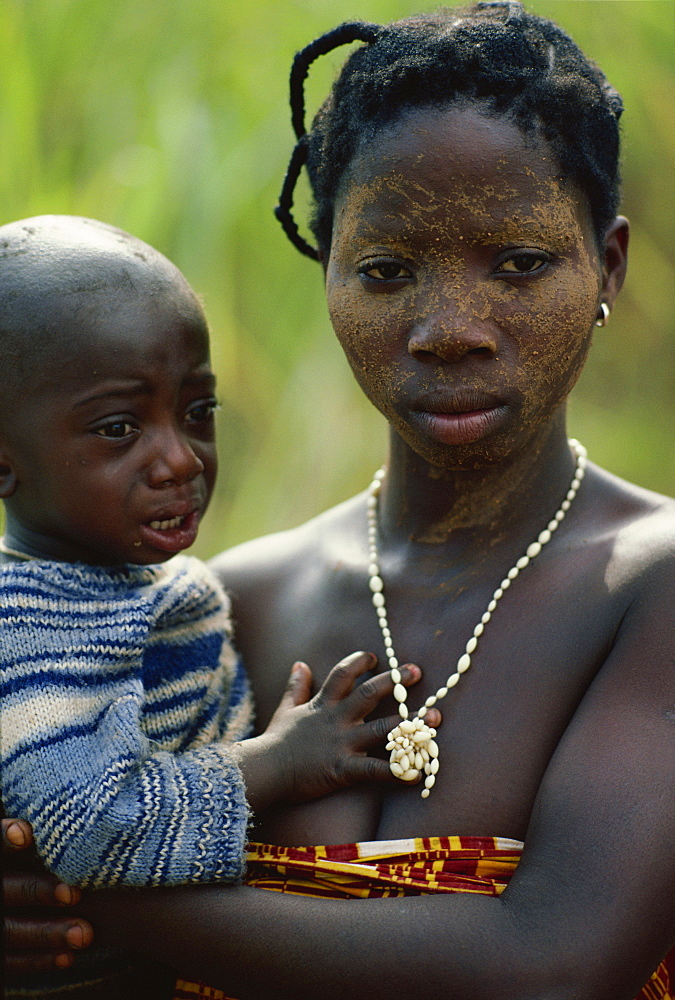 Yacouba woman aged 18, with face covered with tree resin and red pepper to ease toothache, wearing ivory necklace, holding child, Man region, Ivory Coast, West Africa, Africa