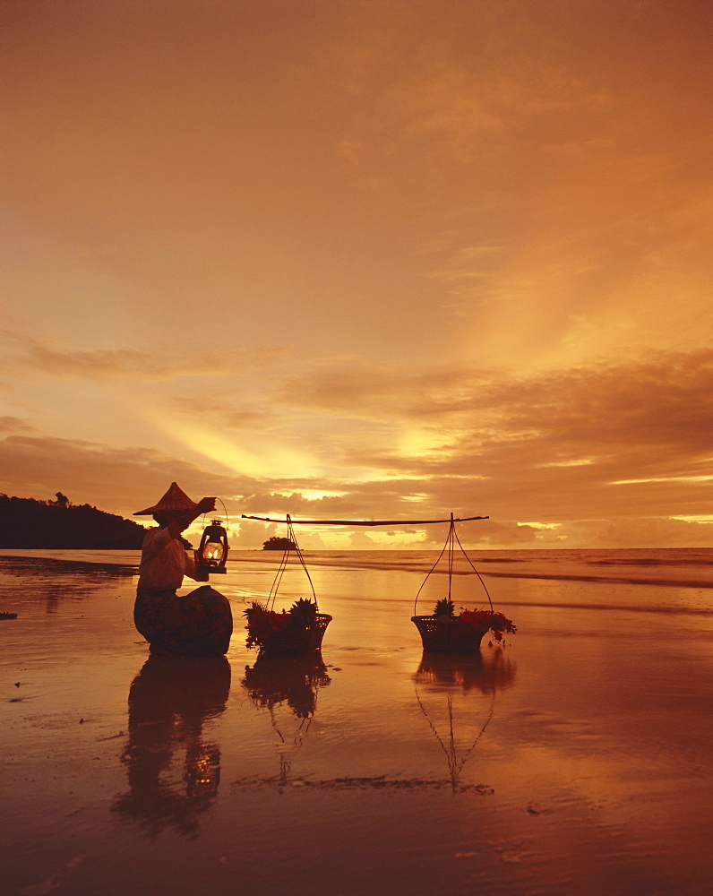 Woman with lamp and baskets on the beach, Phuket, Thailand