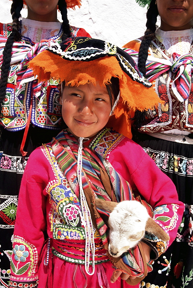 Portrait of a local smiling Peruvian girl in traditional dress, holding a young animal, Cuzco, Peru, South America