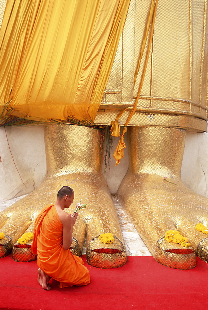 Buddhist monk kneeling in prayer at the feet of a statue of the standing Buddha, Wat Intharawihan, Bangkok, Thailand, Southeast Asia, Asia