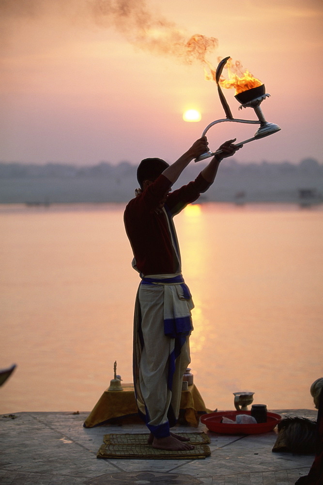 Hindu man worshipping in front of setting sun, River Ganges (Ganga), Varanasi (Benares), Uttar Pradesh state, India, Asia