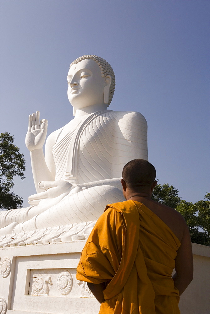 Monk standing in front of the great seated figure of the Buddha, Mihintale, Sri Lanka, Asia