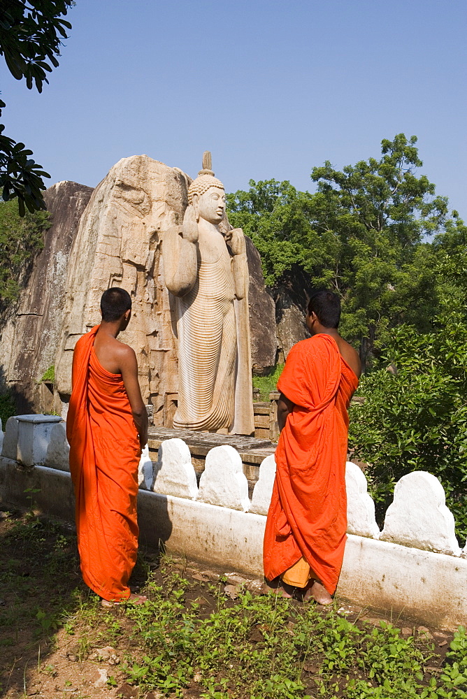 Buddhist monks in front of the giant standing statue of the Buddha dating from the 5th century, Aukana, Sri Lanka, Asia