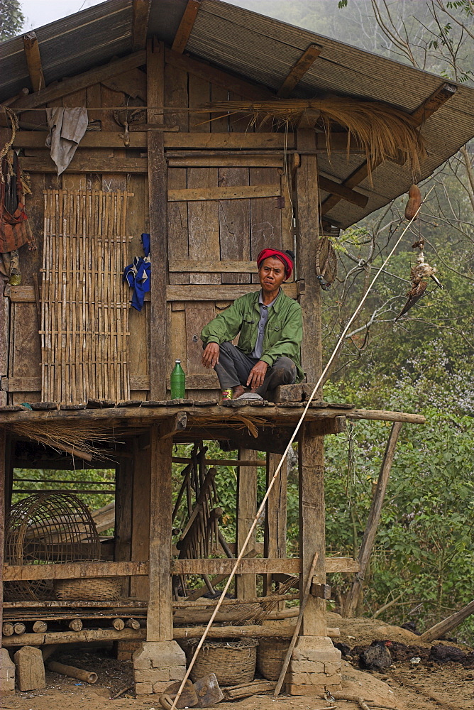 Akha man sitting outside stilted house, Nun Lin Kong village (Akha Tribe), Kengtung (Kyaing Tong), Shan state, Myanmar (Burma), Asia