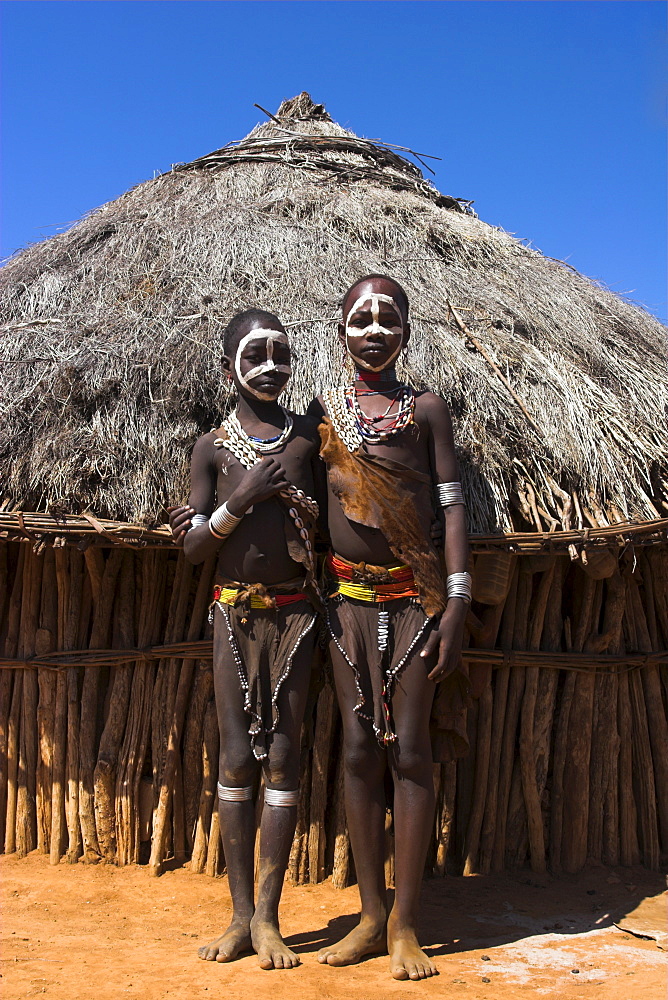 Hamer girls standing in front of house, wearing traditional goat skin dress decorated with cowie shells, Dombo village, Turmi, Lower Omo valley, Ethiopia, Africa