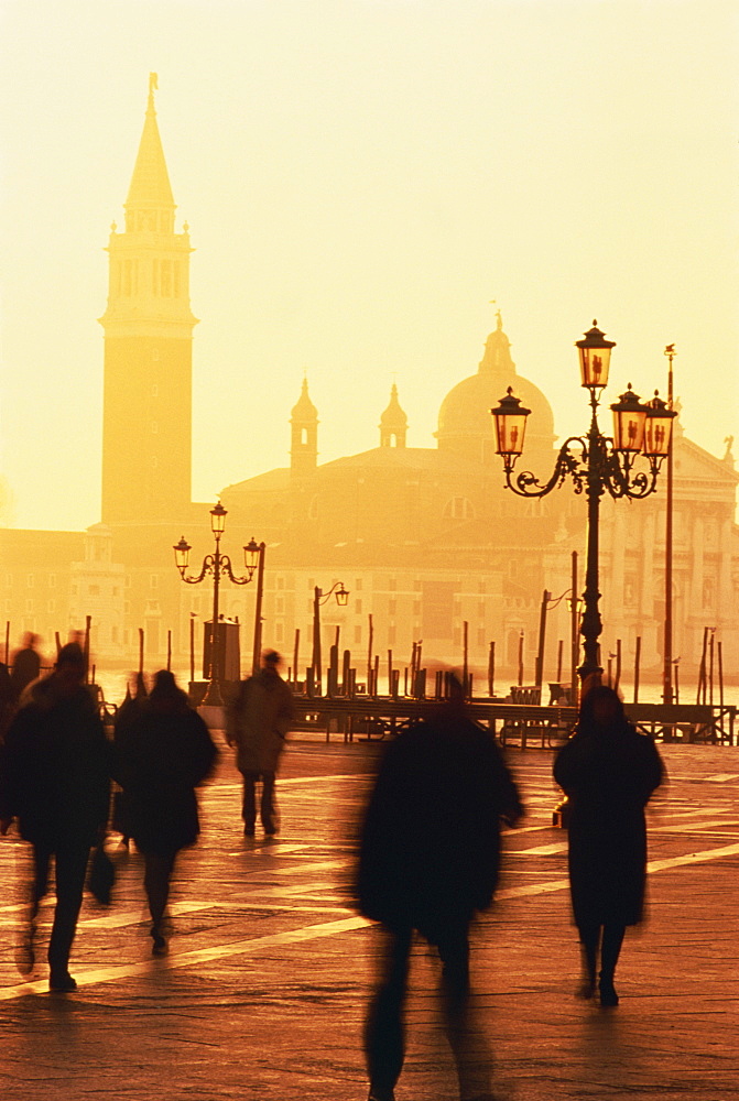 Commuters rushing across St. Mark's Square at sunrise after alighting from ferry with San Giorgio Maggiore in background. Venice, Veneto, Italy, Europe