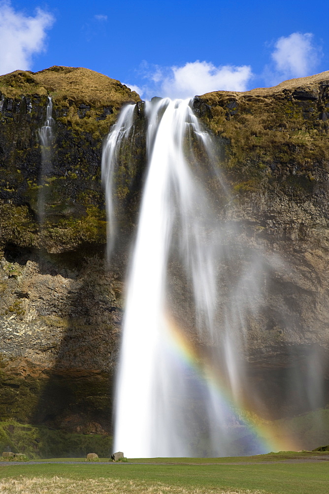 Seljalandsfoss Waterfall tumbling over towering cliffs in bright sunlight with rainbow at the base of the waterfall, near Hella, Southern Iceland, Iceland, Polar Regions