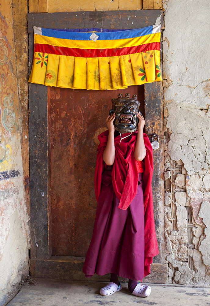 Young Buddhist holding holding carved wooden mask over his face at the Tamshing Phala Choepa Tsechu, near Jakar, Bumthang, Bhutan, Asia