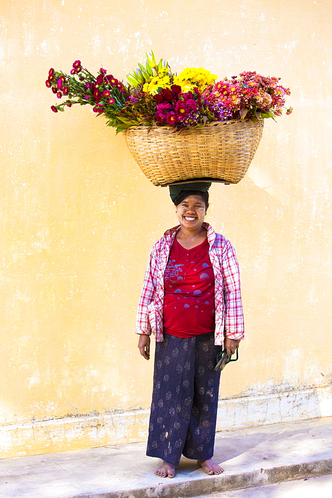 Local woman with thanakha traditional face painting, carrying a large basket of fresh flowers on her head, Shwezigon Paya, Nyaung U, Myanmar (Burma), Asia