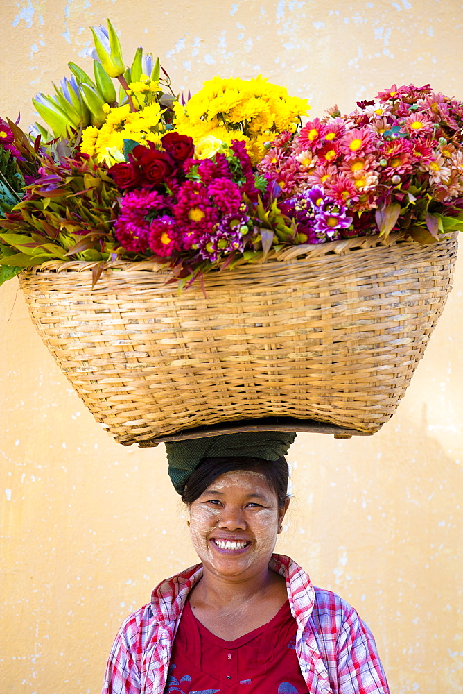 Local woman with thanakha traditional face painting, carrying a large basket of fresh flowers on her head, Shwezigon Paya, Nyaung U, Myanmar (Burma), Asia