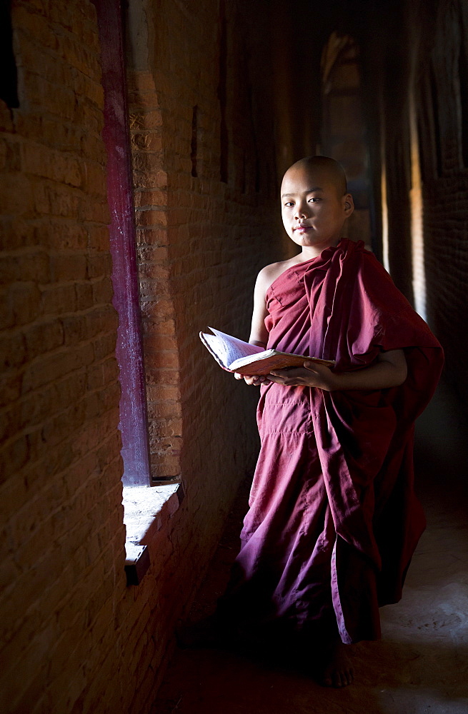 Novice Buddhist monk reading Buddhist scriptures in the light of a window in one of the many temples of Bagan, Myanmar (Burma), Asia