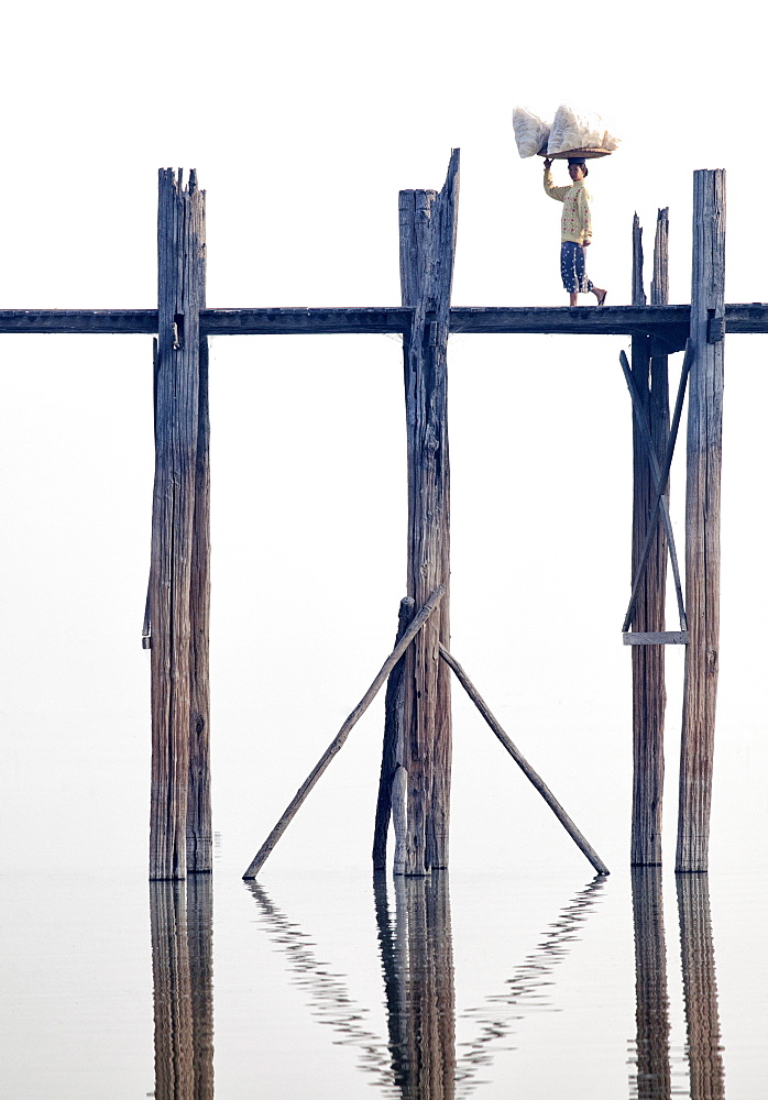 Local woman carrying goods on her head across U Bein Bridge, the world's longest teak foot bridge spanning 1300 yards over Taungthaman Lake, Amarapura, near Mandalay, Myanmar (Burma), Asia