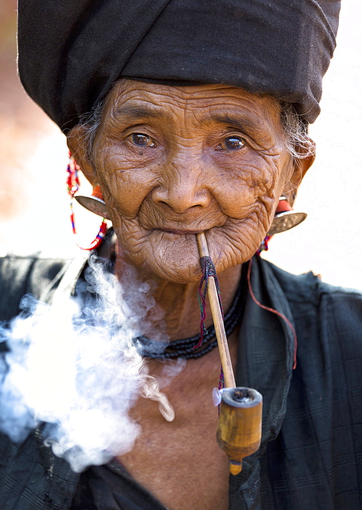 Woman of the Ann tribe in traditional black dress smoking a pipe outside a hill village near Kengtung (Kyaingtong), Shan State, Myanmar (Burma), Asia