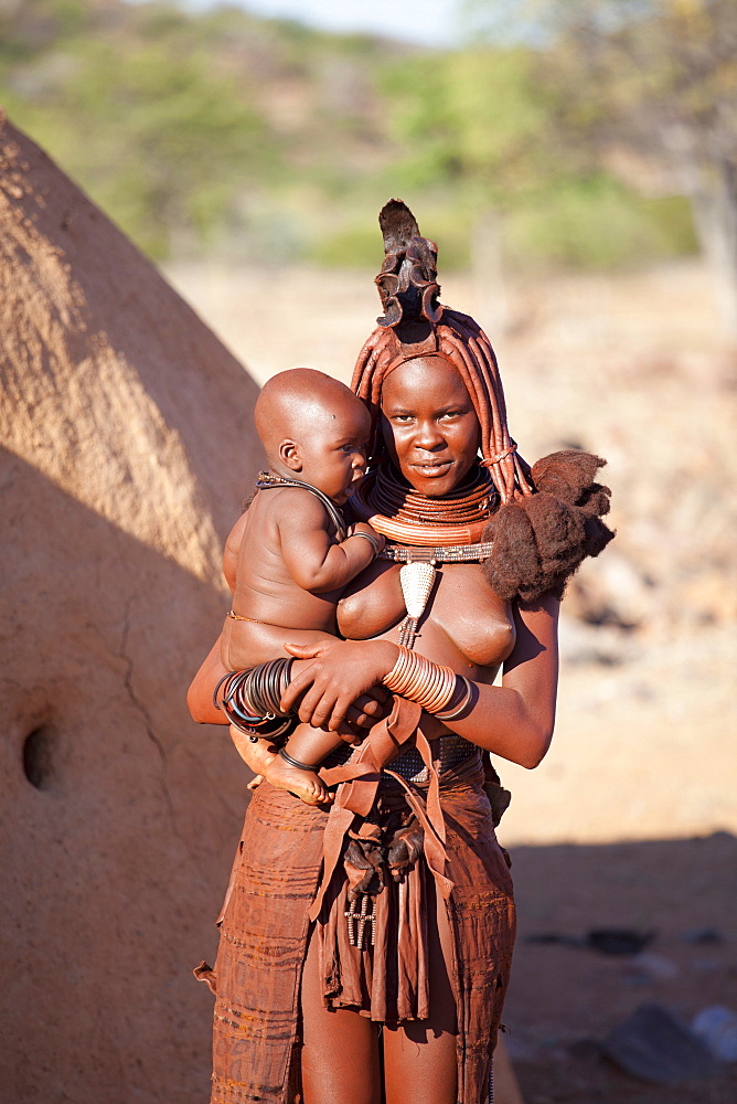 Young Himba woman, with baby, wearing traditional dress and jewellery and with her skin covered in Otjize, a mixture of butterfat and ochre, Kunene Region, formerly Kaokoland, Namibia, Africa