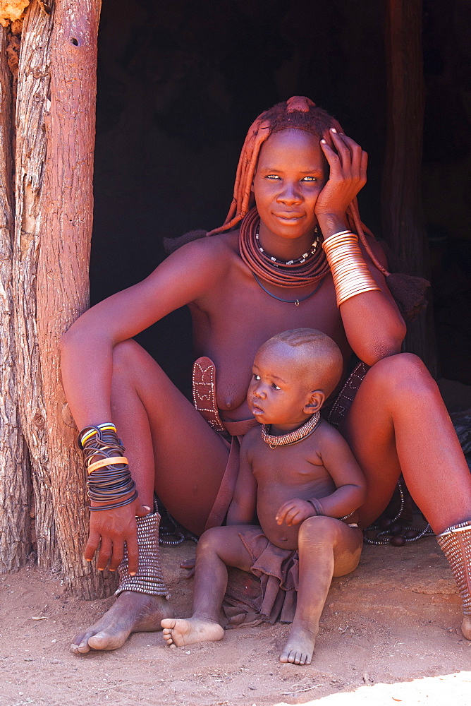 Young Himba woman, with baby, wearing traditional dress and jewellery and with her skin covered in Otjize, a mixture of butterfat and ochre, Kunene Region, formerly Kaokoland, Namibia, Africa