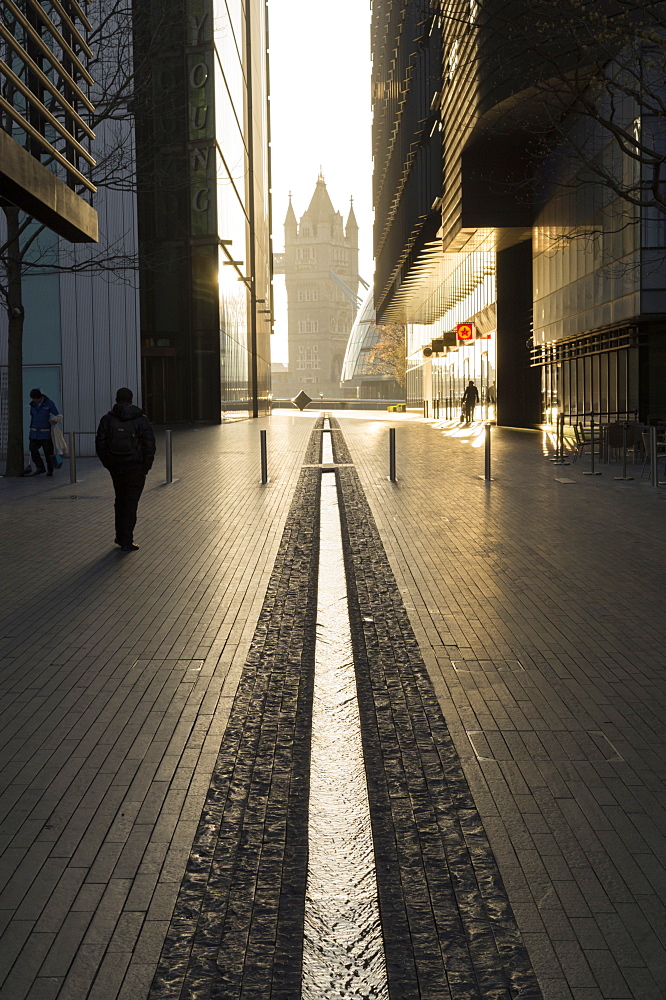 Ornamental stream flows through More Place with Tower Bridge at end of tunnel of buildings, London, England, United Kingdom, Europe