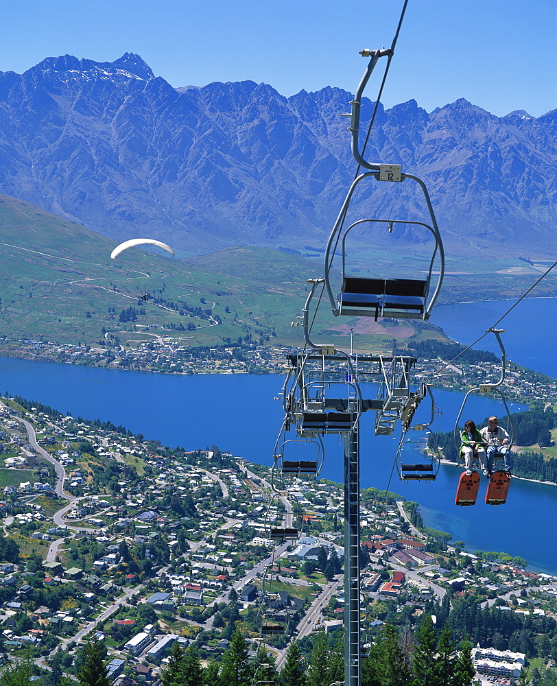 Tourists on a chair lift with Lake Wakatipu, the Remarkable Mountains and Queenstown, South Island, New Zealand, Pacific