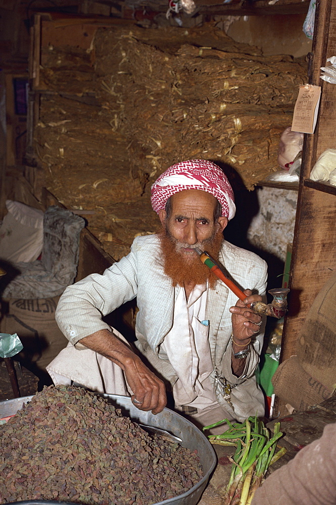 Portrait of an elderly shopkeeper with henna dyed beard, smoking a pipe, Djiblah, Yemen, Middle East