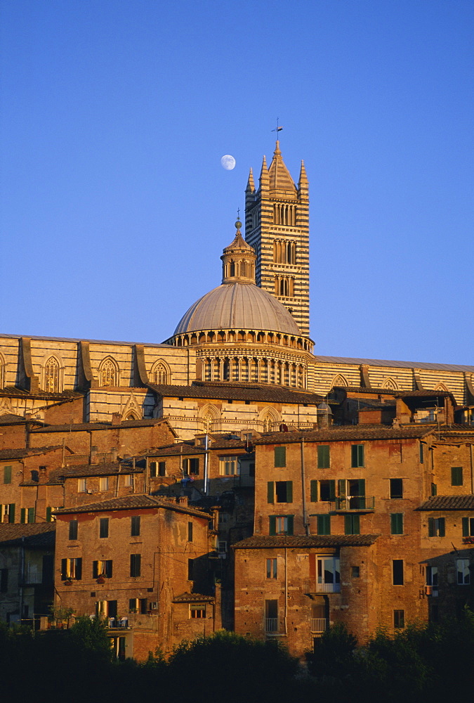 Moon in the sky above cathedral and houses clustered below at sunset, Siena, Tuscany, Italy, Europe