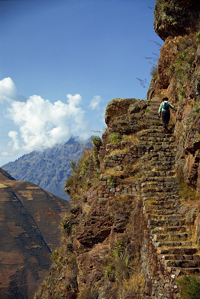 A walker climbs the steps on a narrow path along the edge of a cliff at an Inca site in the Urubamba Valley, Pisac, Peru, South America