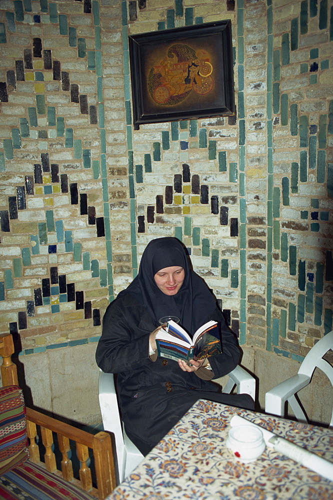 Western tourist in traditonal dress, reading book in tea house, Kerman, Iran, Middle East